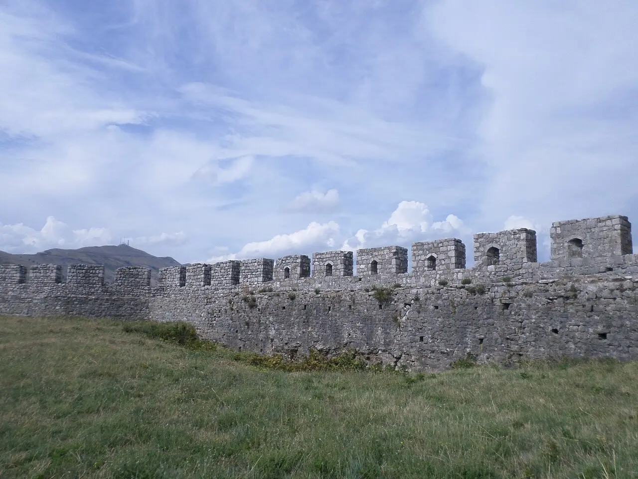 The high stone walls and arched gate of Rozafa Castle under a blue sky