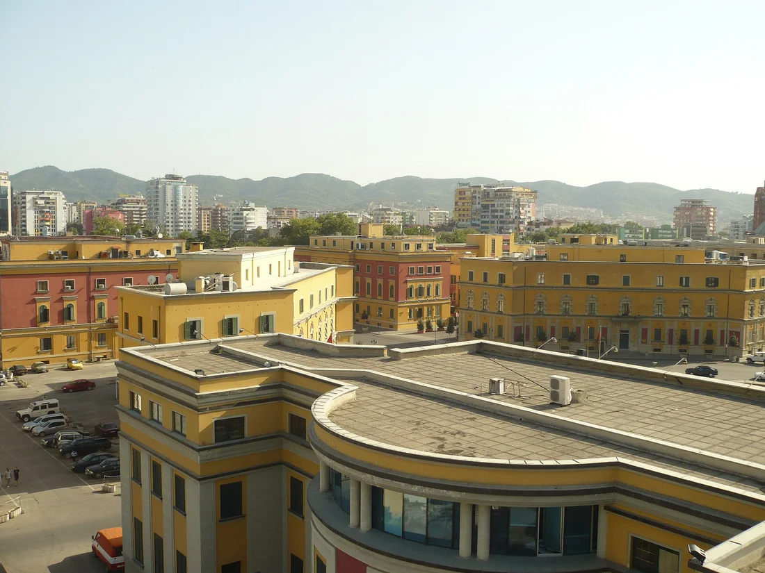 Tirana's rooftops and the yellow ministry buildings seen from the Clock Tower with hills behind