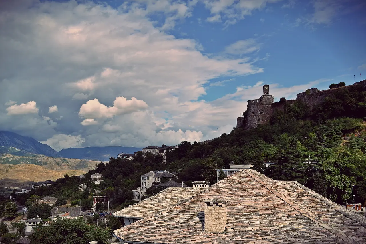 The castle and clock tower of Gjirokaster above the stone-slate roofs of the old town under dramatic clouds