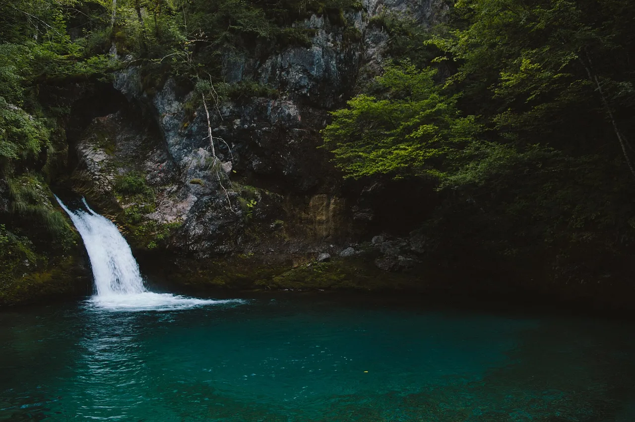 The vivid turquoise pool of the Blue Eye of Theth with a small waterfall feeding it