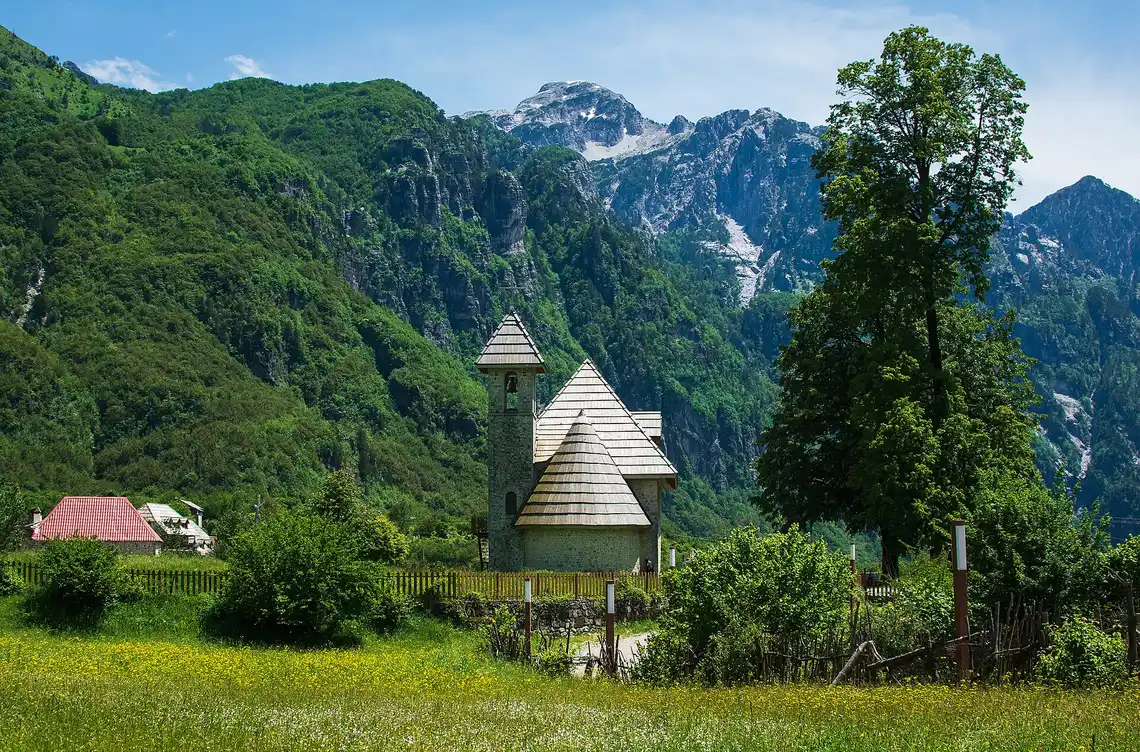 The stone Catholic church of Theth standing in a green meadow below the peaks