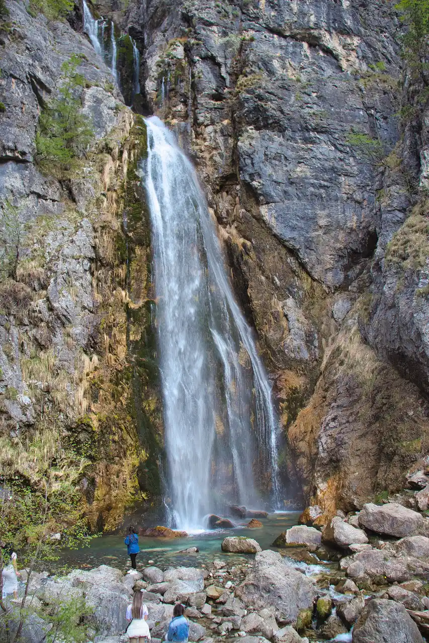The Grunas waterfall dropping over a rock face into a pool among green trees near Theth