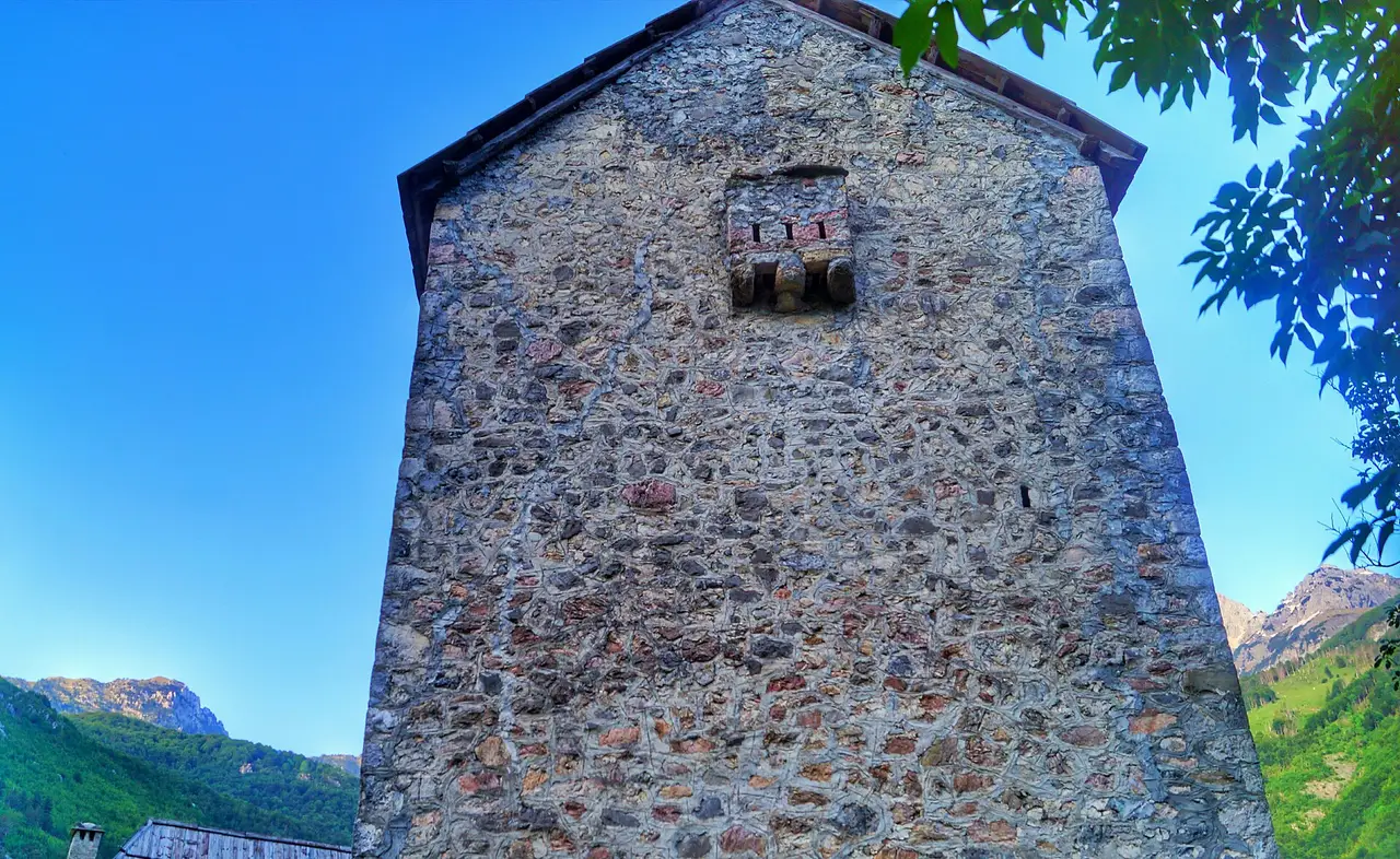 The stone Lock-in Tower of Theth standing in a meadow below the mountains