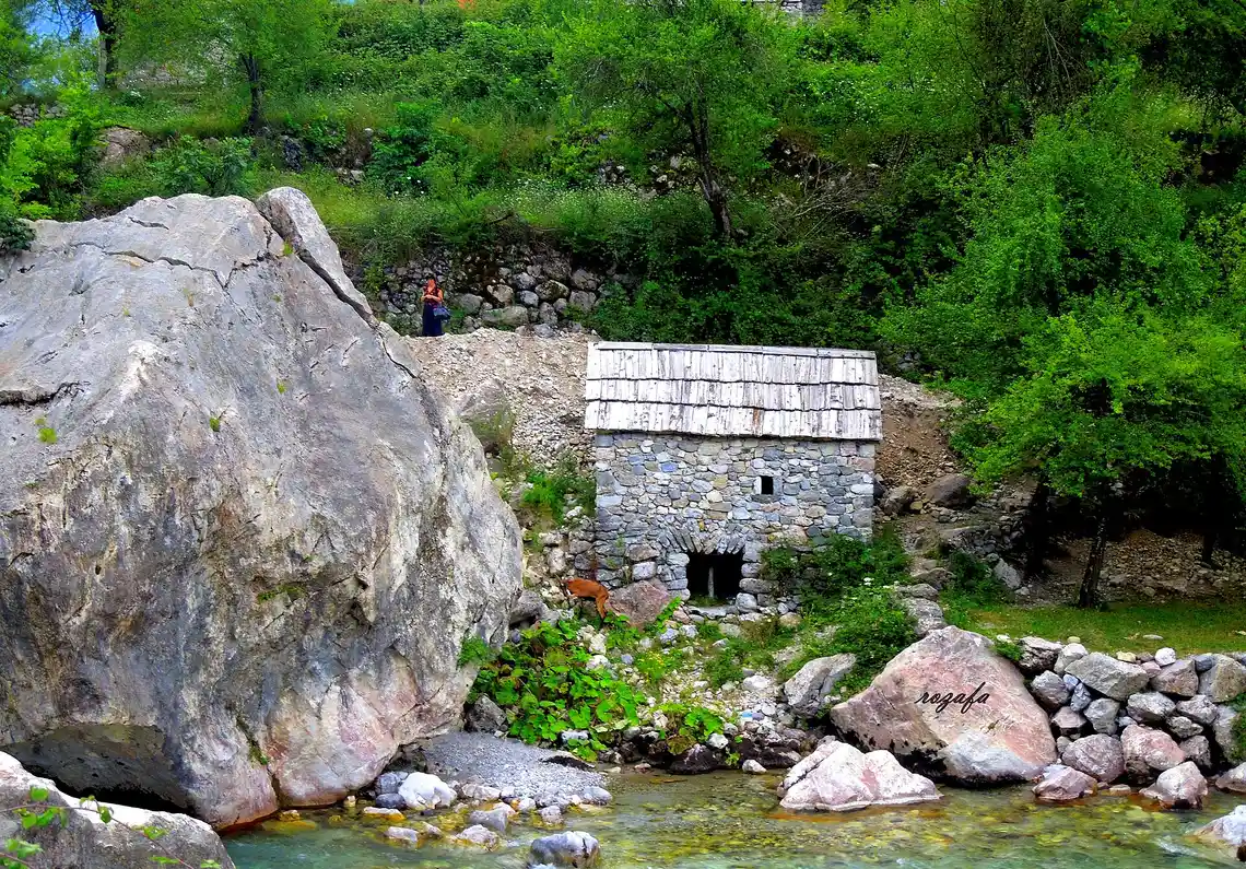 Stone houses scattered across green meadows below the mountains in Theth