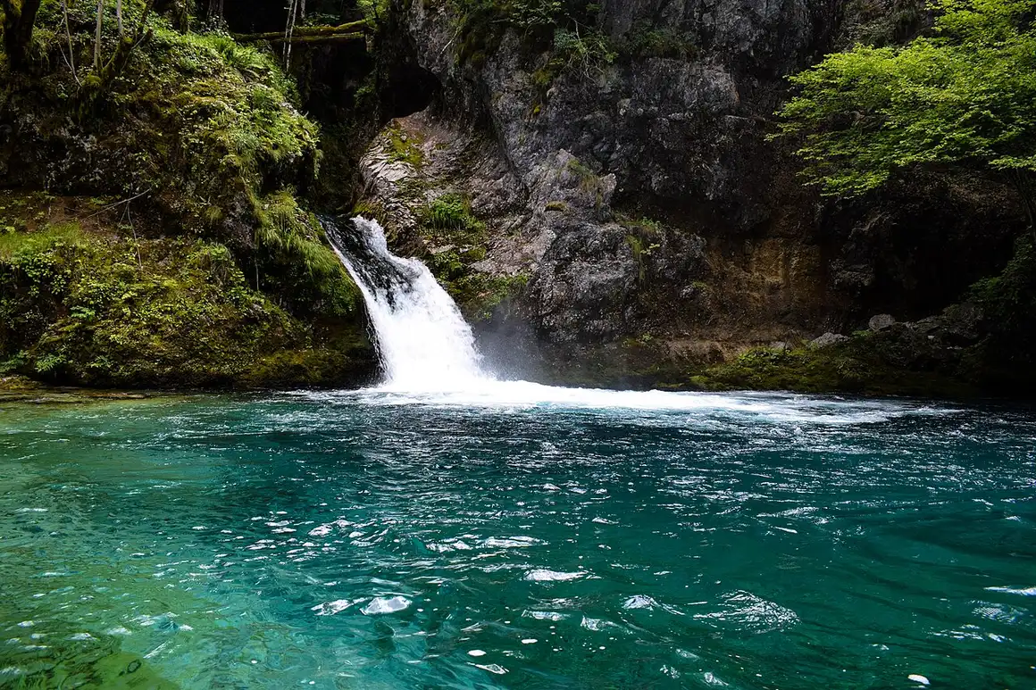 The vivid turquoise pool of the Blue Eye of Theth surrounded by rocks and forest