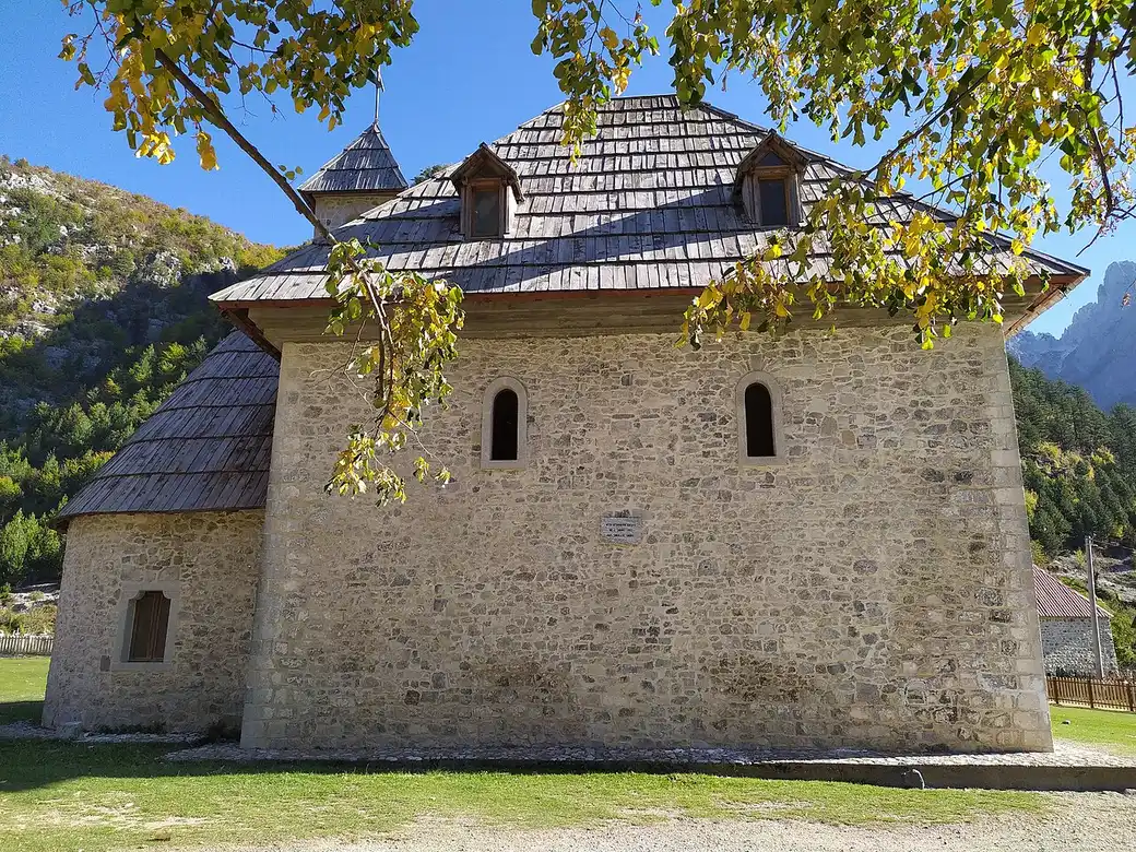 The stone church of Theth village standing in a green meadow below the Albanian Alps