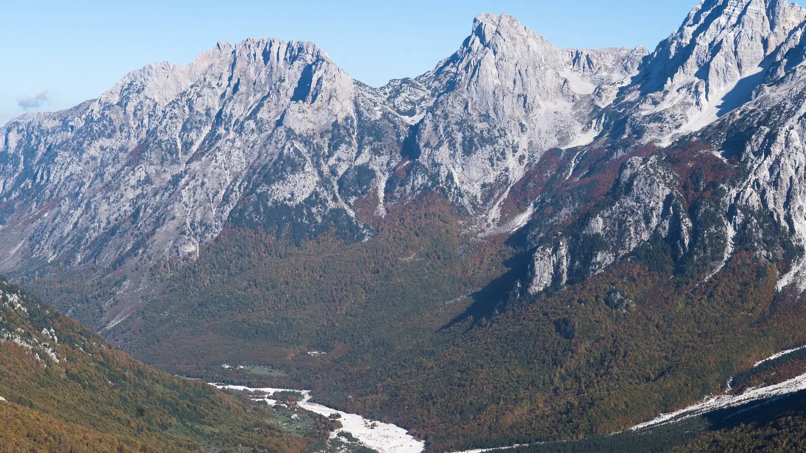 Wide autumn view over the pale riverbed and valley floor of Valbona, framed by bare limestone peaks of the Albanian Alps