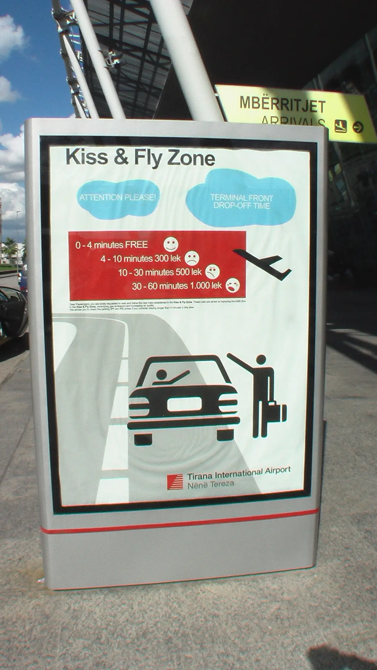A Kiss and Fly drop-off price sign at Tirana airport showing free for 0-4 minutes, then 300, 500 and 1000 lek bands