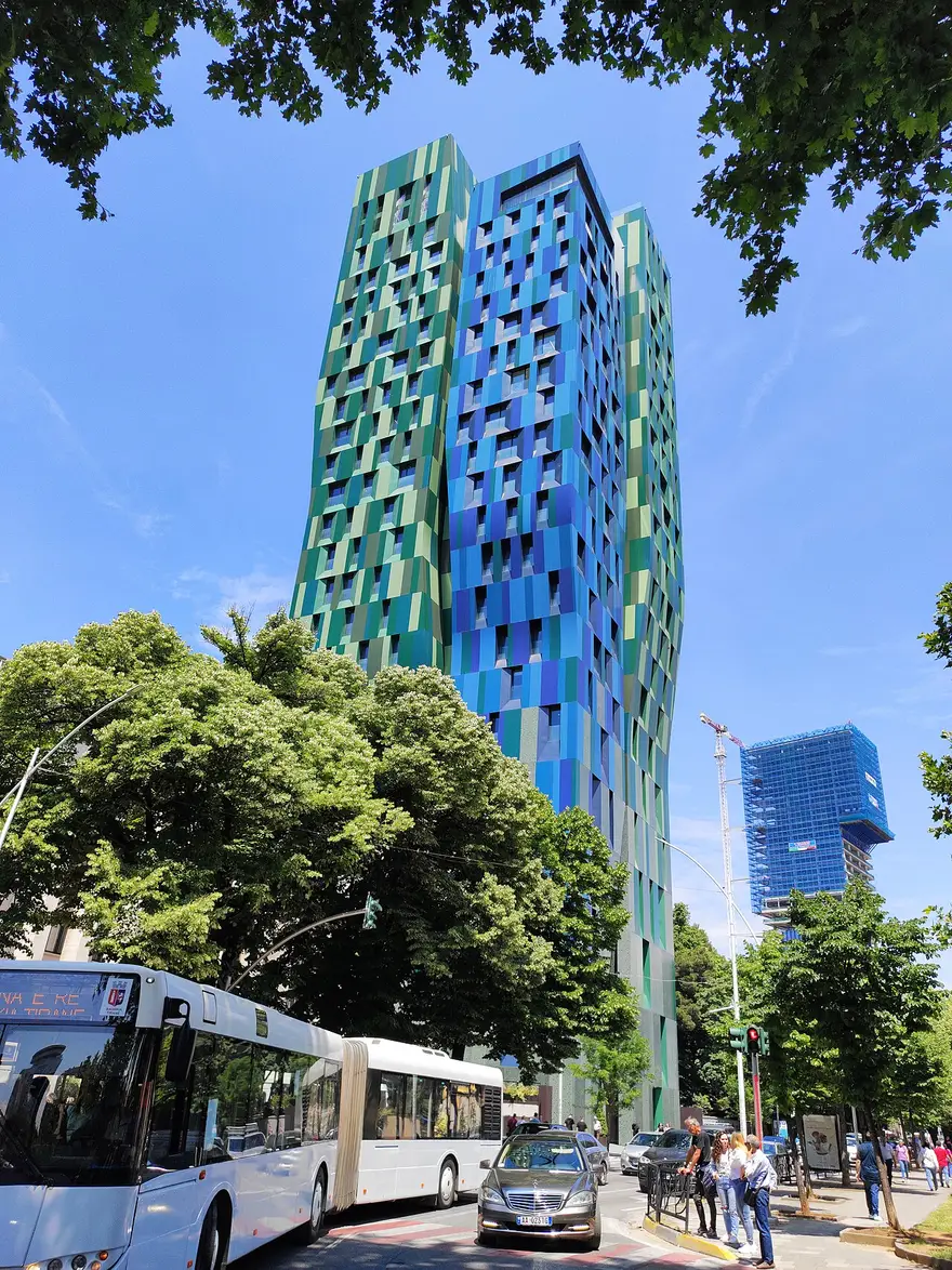 A colourful modern skyscraper in central Tirana with a city bus and pedestrians at street level