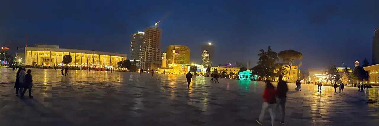 Skanderbeg Square in Tirana at dusk with the opera house, towers and people strolling across the plaza