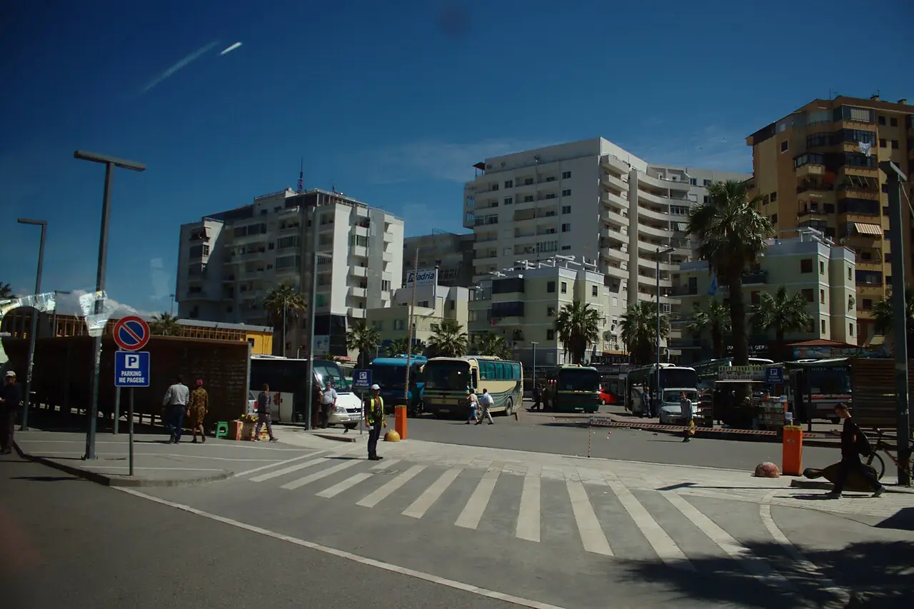Buses and minibuses parked at the main bus station in Durres with palm trees and apartment blocks behind