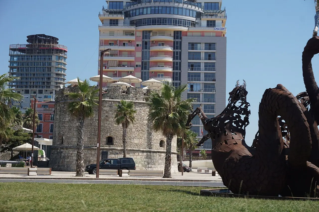 The Venetian Tower and palm trees on the Rruga Taulantia waterfront in Durres, with a modern building behind