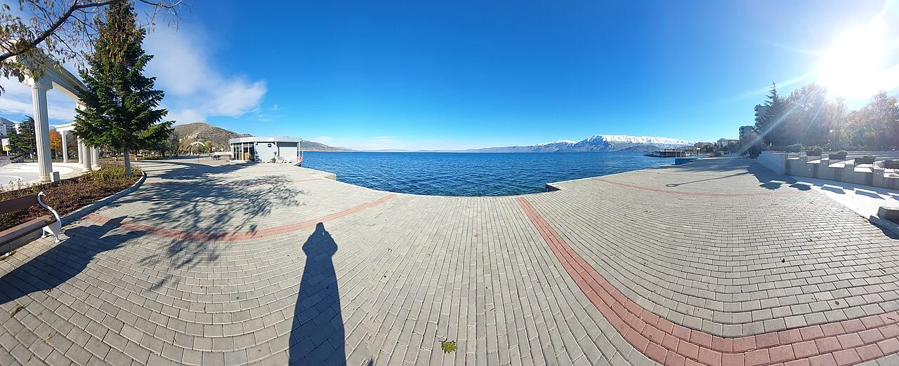 The wide lakefront promenade at Pogradec on the Albanian side of Lake Ohrid, with snow-capped mountains across the water