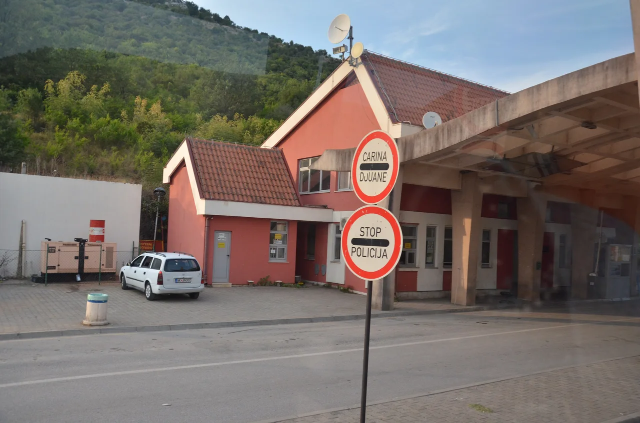 A pink border control building with a tiled roof and a red and white customs and police stop sign at the Božaj crossing