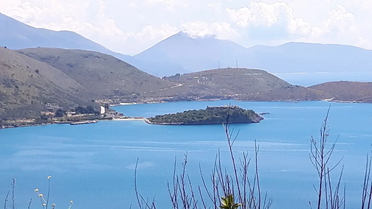 The bay of Porto Palermo seen from the coast road above, the wooded castle peninsula sitting in flat turquoise water