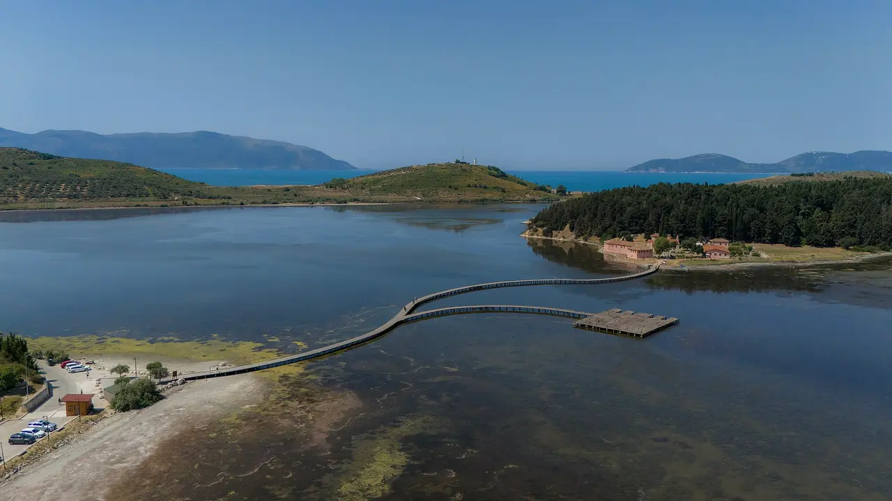 The wooden walkway curving across the shallow Narta lagoon to the wooded Zvernec island, with the Karaburun hills behind
