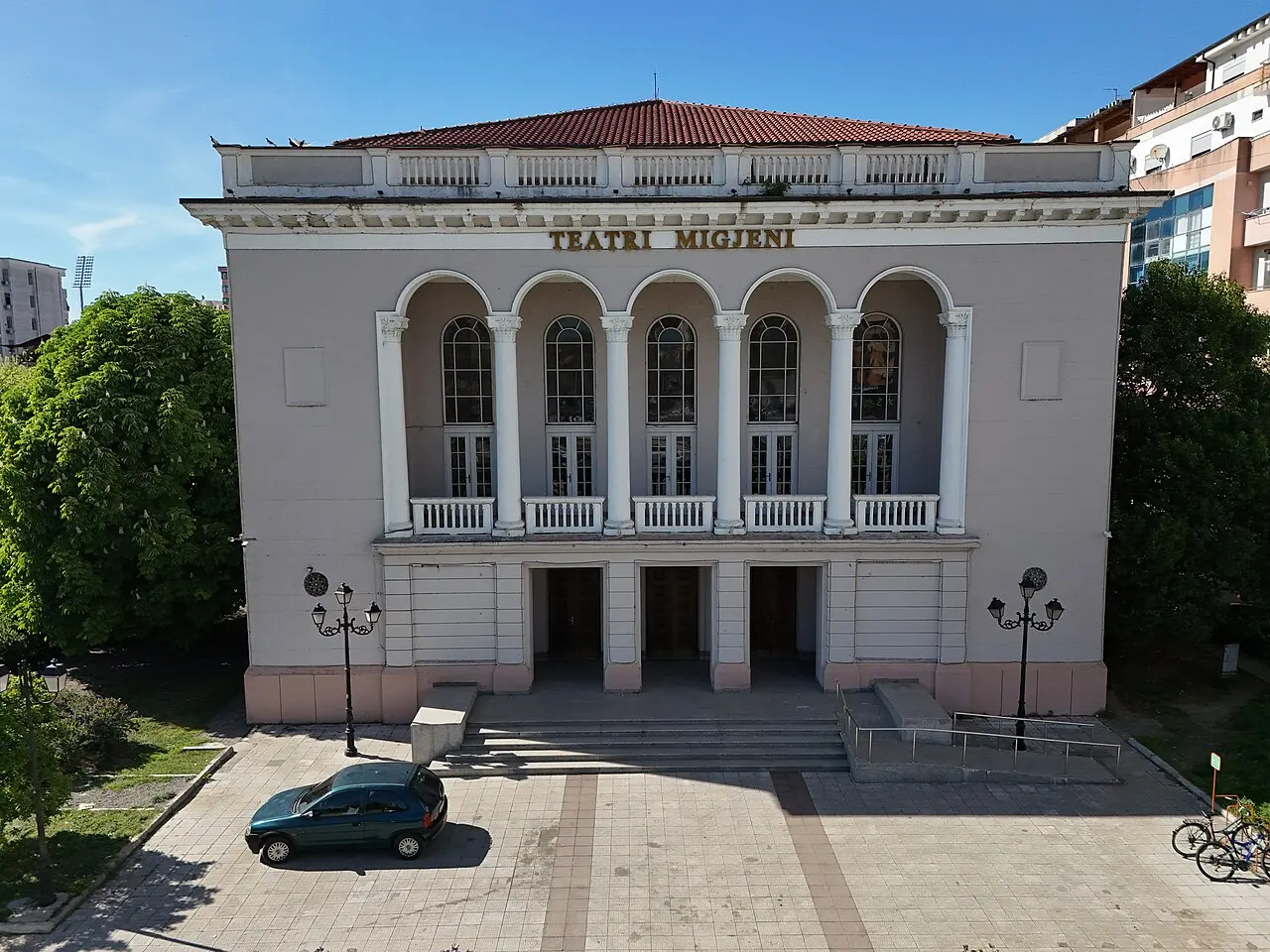 The pale facade of the Migjeni Theatre in Shkodra with its arched upper loggia and the name Teatri Migjeni above the columns