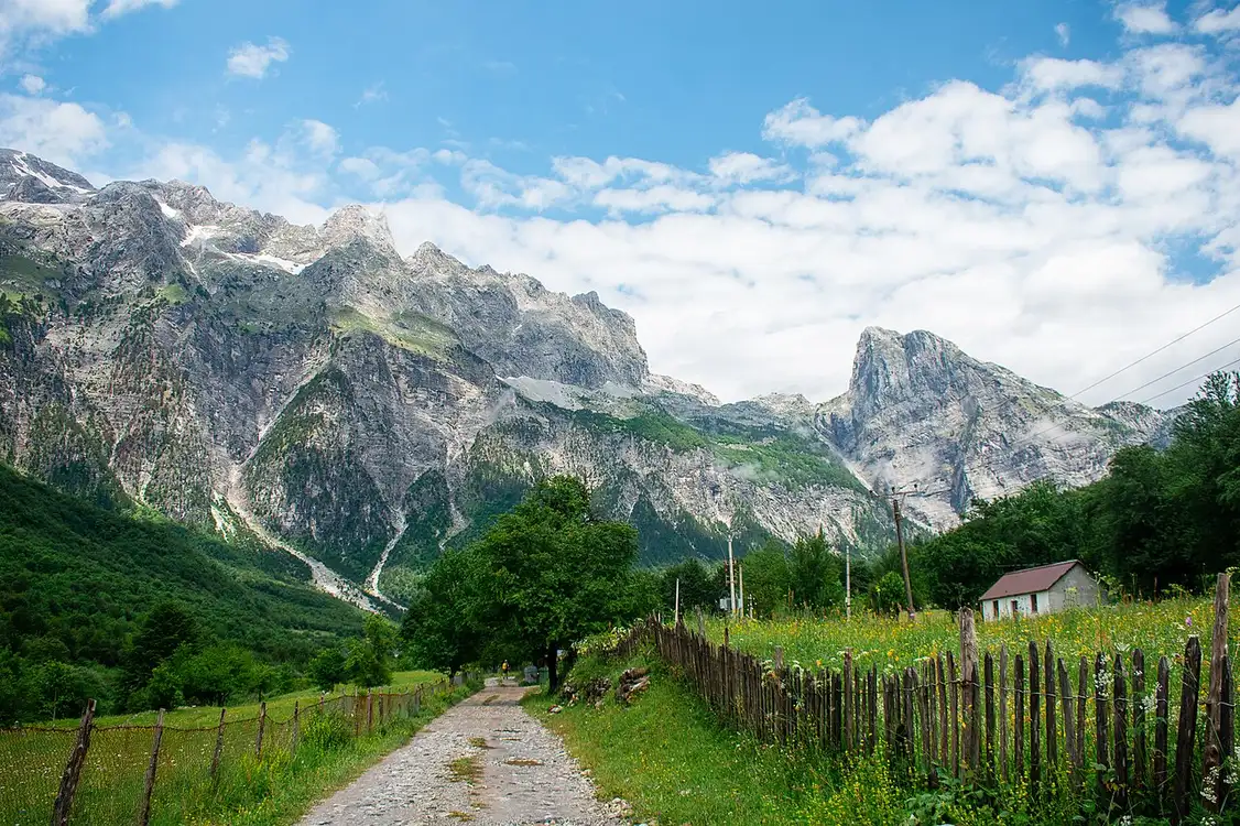 The green Theth valley ringed by the sharp peaks of the Albanian Alps, with meadows and scattered stone houses