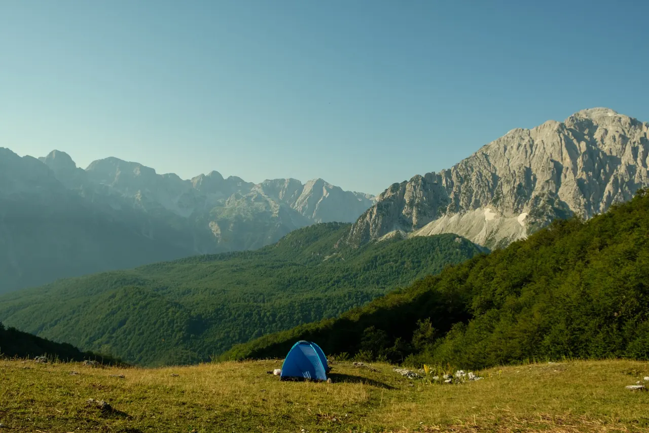 Tent camping beside a stream with alpine peaks behind in Valbona Valley