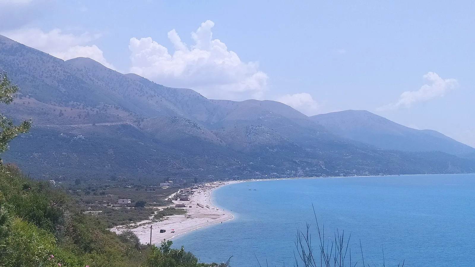 A wide view of the Riviera coastline near Borsh on the Vlora to Saranda road, with a pebble beach curving below green mountains
