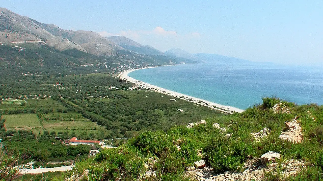 The long curving beach and coastline at Himara seen from a hillside above the SH8 coastal road, with the Ceraunian Mountains behind