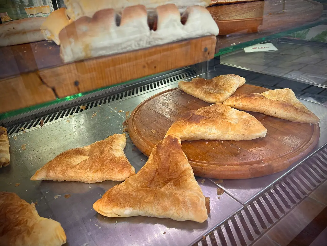 Golden triangular byrek pastries in a bakery display case in Tirana