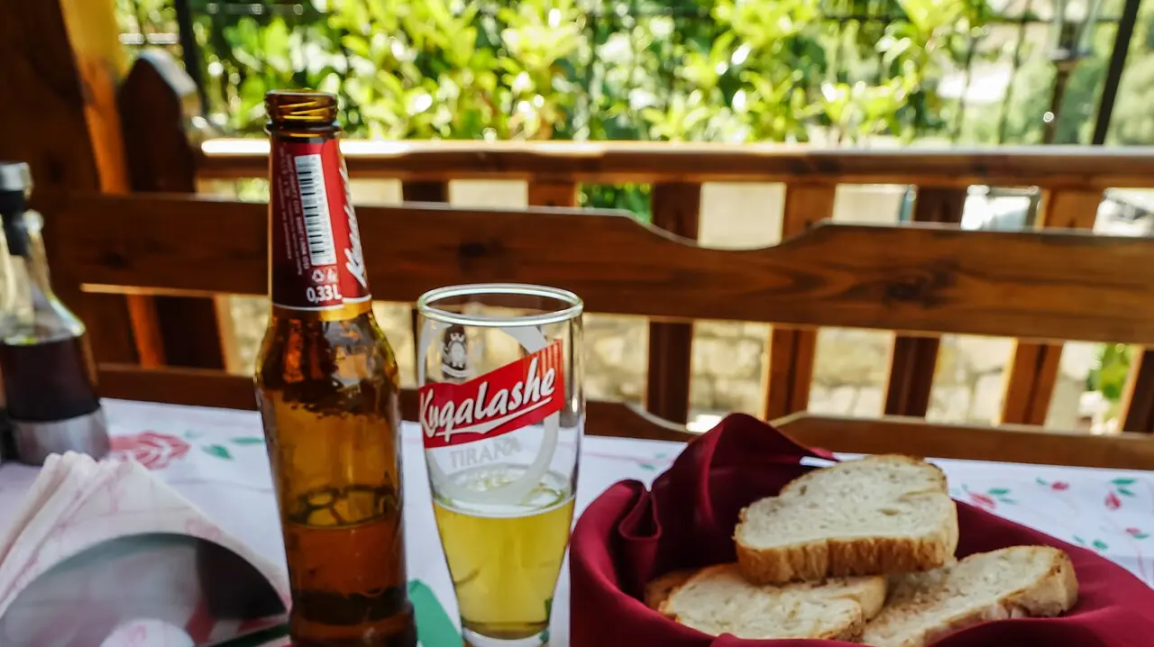 A bottle of Albanian beer, a glass and a basket of bread on a wooden guesthouse balcony in Berat