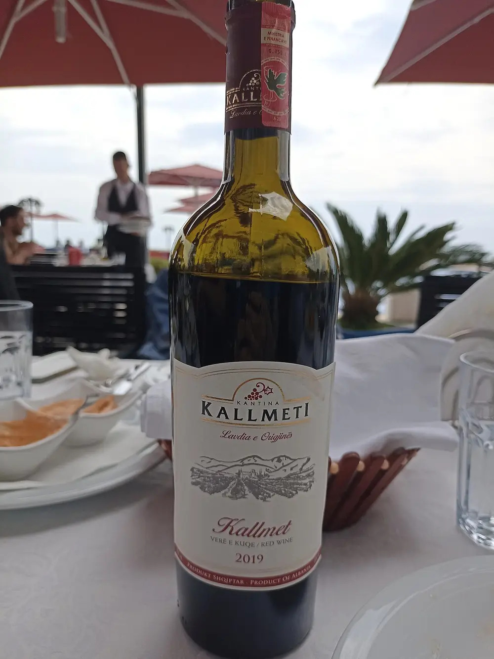 A bottle of Albanian Kallmet red wine on a white-clothed restaurant table by the sea