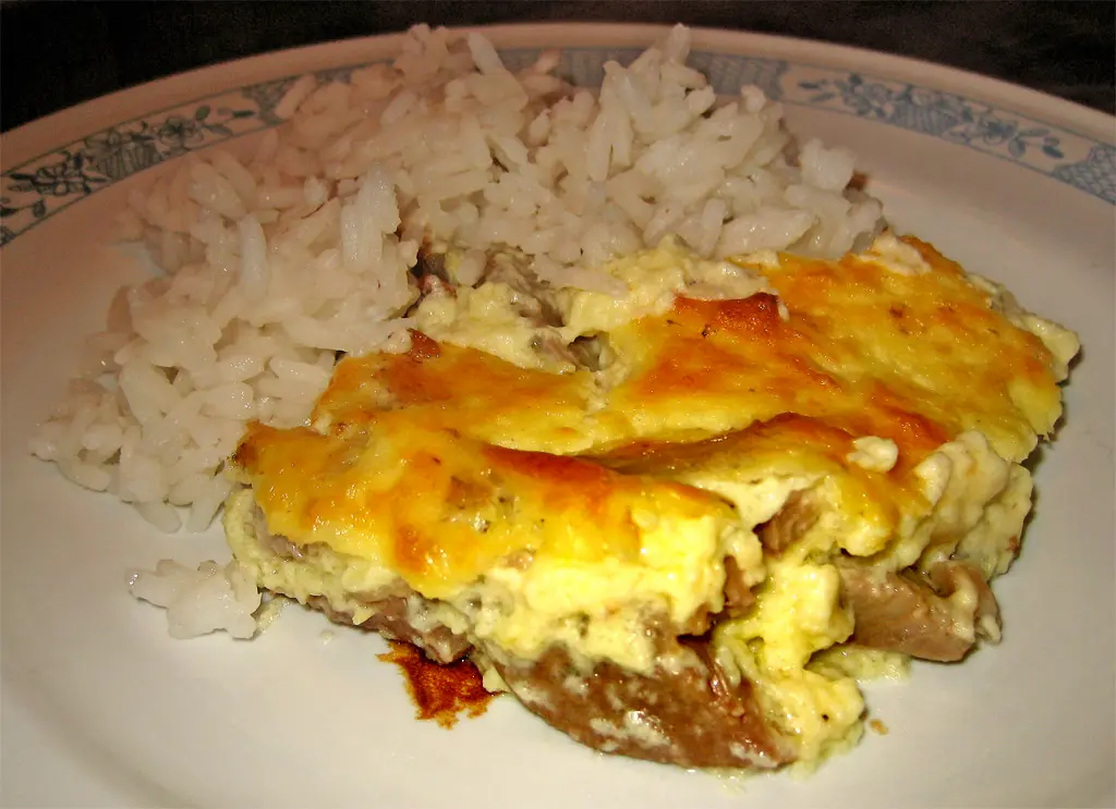 A plate of tavë kosi, baked lamb under a golden yogurt-and-egg custard, served with white rice