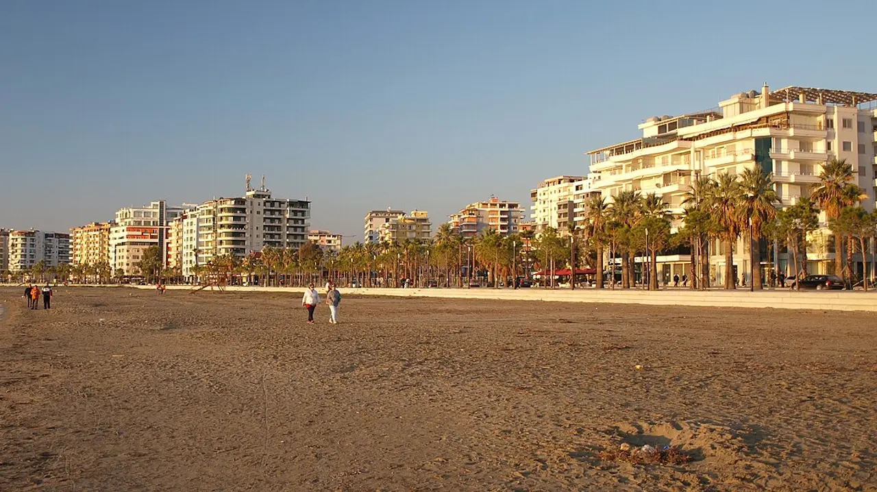 The Lungomare promenade in Vlora at golden hour with rows of seafront hotels, palm trees and a wide sandy beach