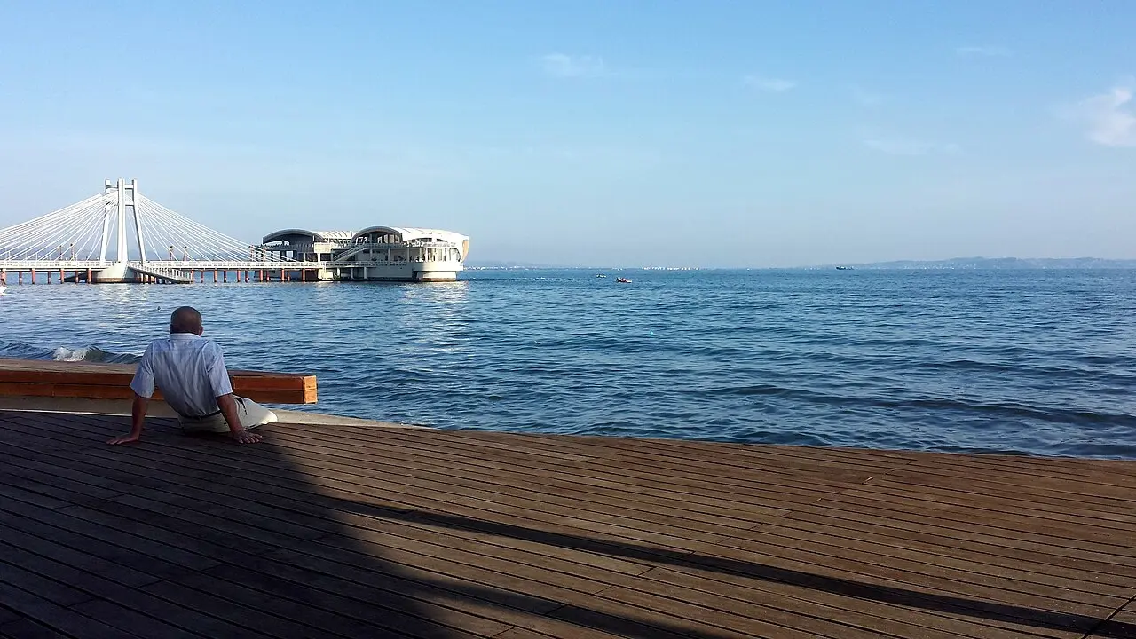 The wooden seafront boardwalk in Durres beside calm blue water, with a pier and pavilion in the distance