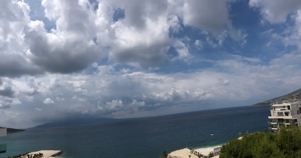 A wide view over Saranda bay from a hillside balcony, with the Ionian Sea and the coastline curving into the distance