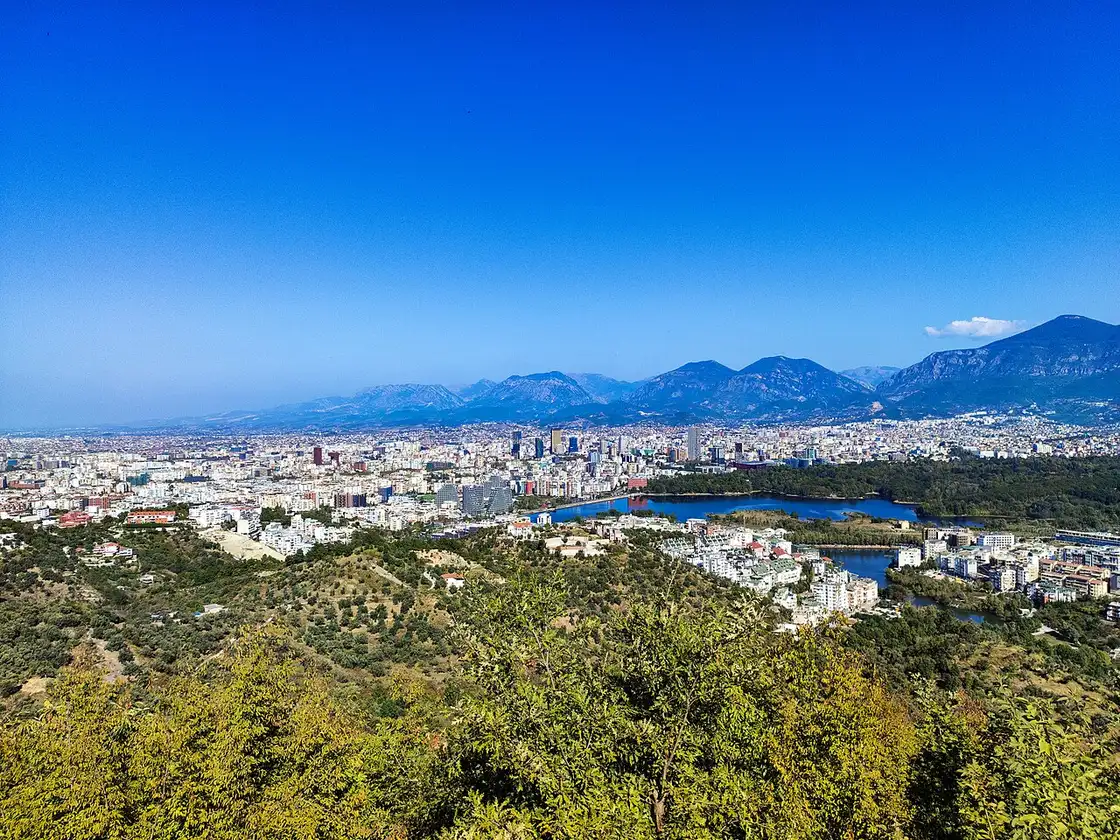 The modern Tirana skyline set against green hills and mountains under a clear blue sky