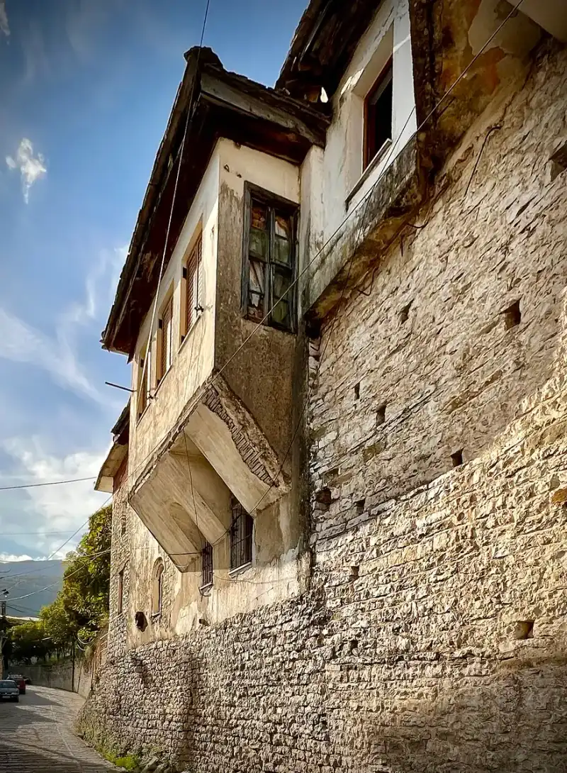 Tall stone facade of a traditional Gjirokaster house with small windows and a heavy slate roof
