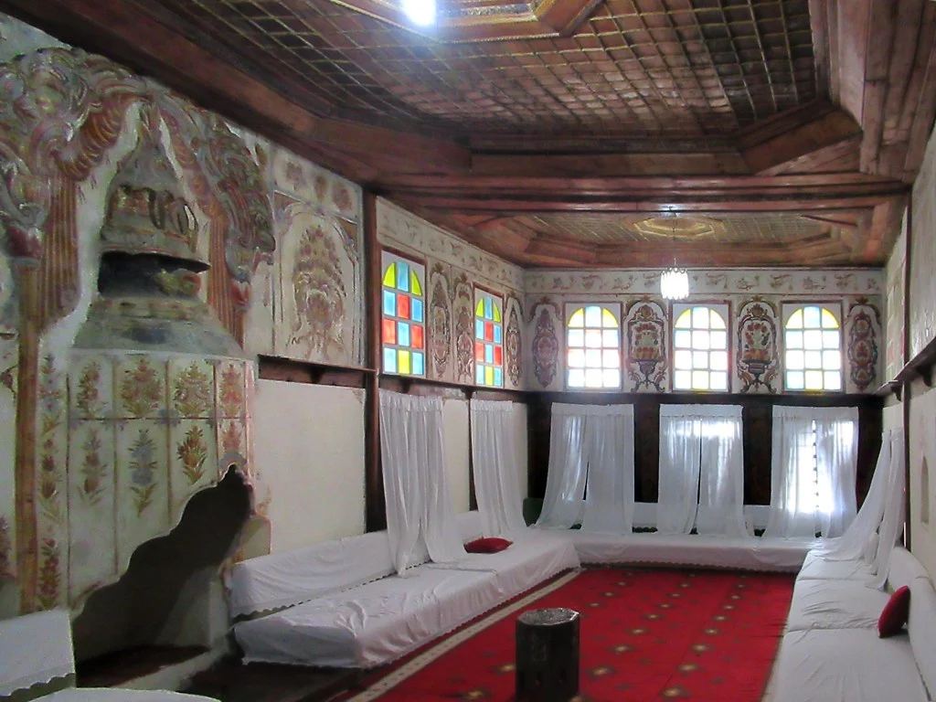 Guest room in the Zekate House museum in Gjirokaster with a carved wooden ceiling, painted walls, a tiled fireplace and low white divans