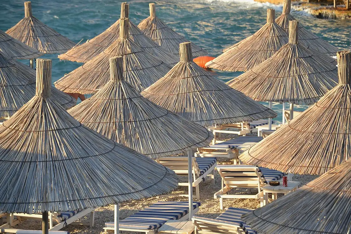 Rows of straw parasols and blue-striped sun-loungers on a Ksamil beach in golden evening light