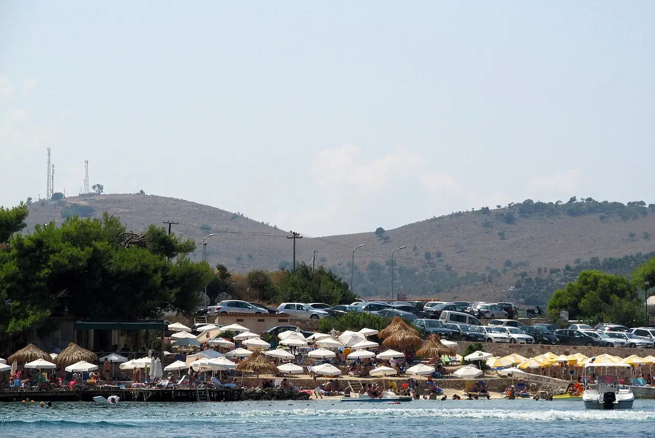 A Ksamil beach packed with straw parasols and sun-loungers, with a full car park on the slope behind
