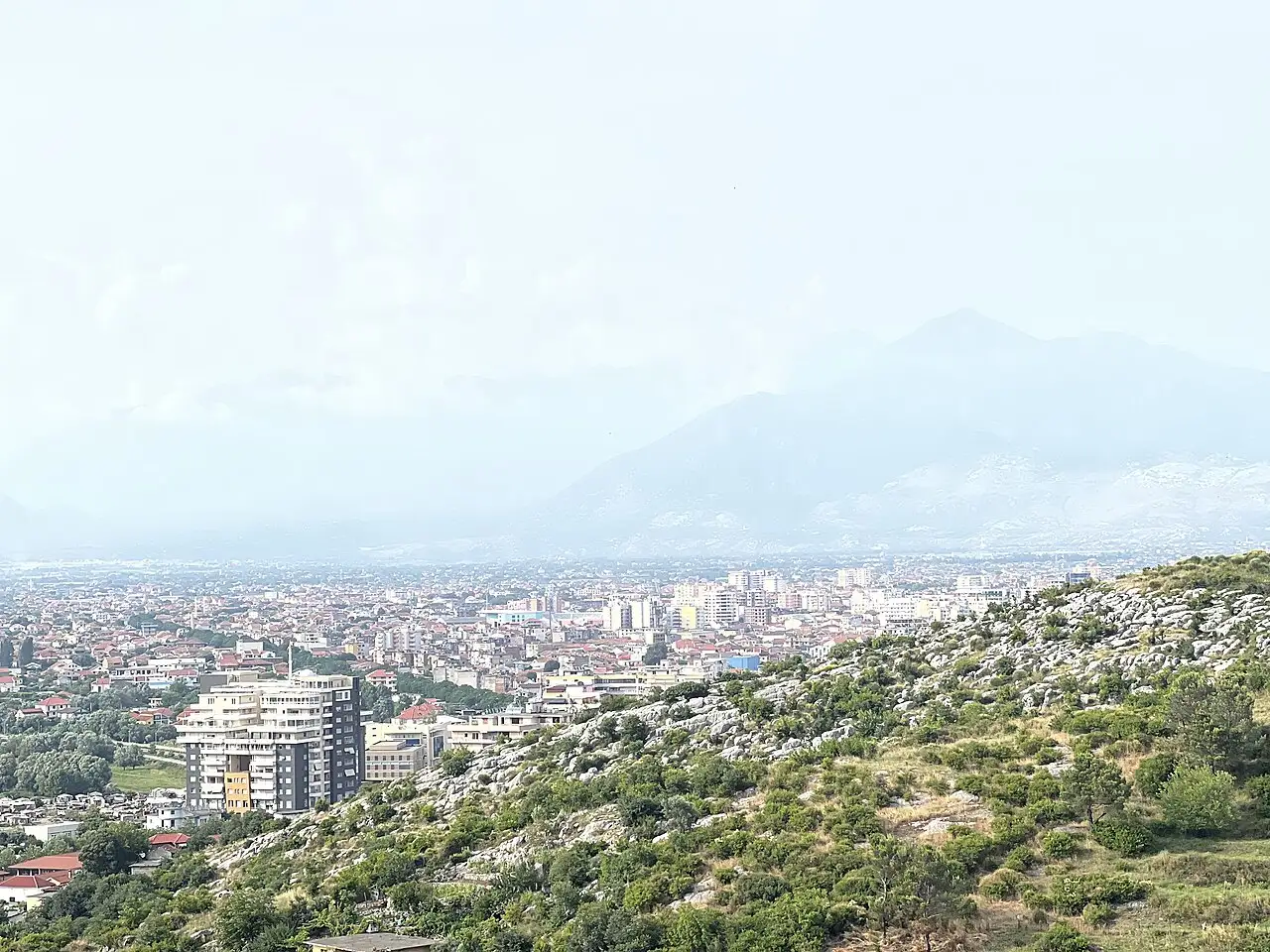 A hazy view over the rooftops of Shkodra toward the Albanian Alps in the distance