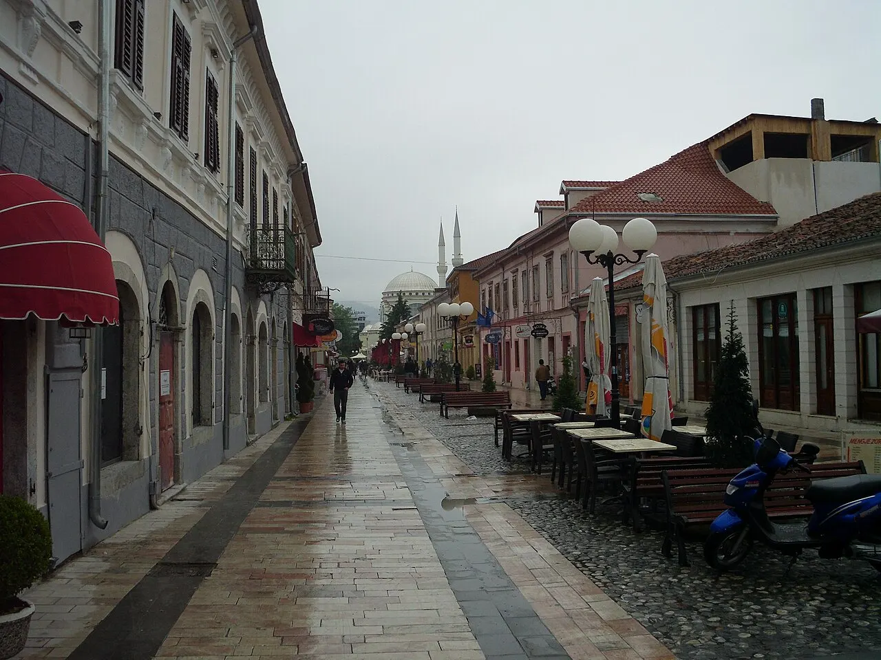 The rainy pedestrian street Rruga Kolë Idromeno in Shkodra with cafe tables and a distant mosque