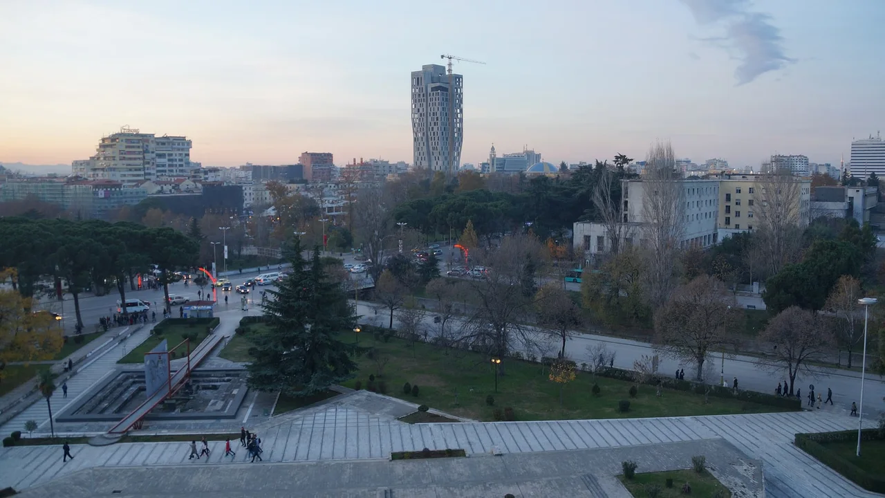 Central Tirana at dusk seen from above: park, traffic circle and a tower under construction