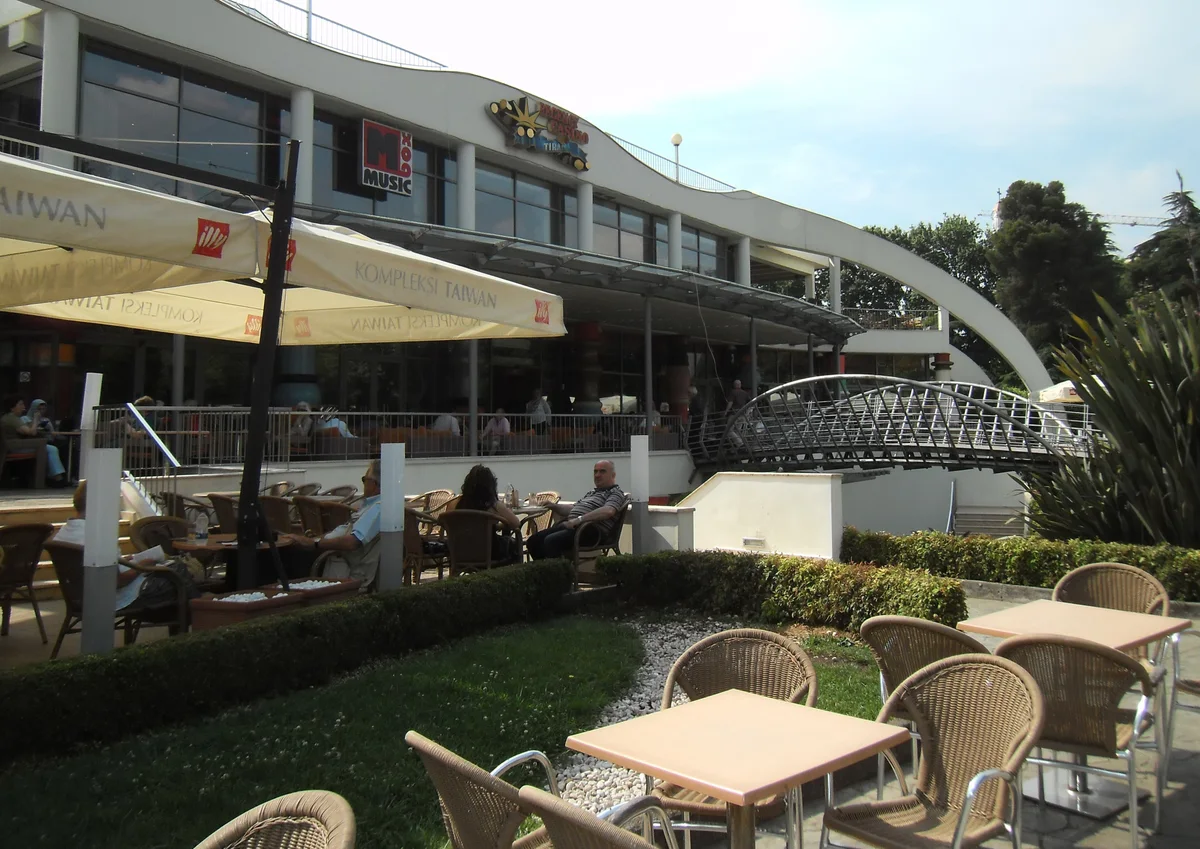 Outdoor cafe terraces with wicker chairs beside a curved building in Tirana